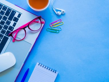 Dizüstü bilgisayar, not defteri, mavi kalem, pembe gözlük ve mavi zemin üzerine kahve gibi ofis aksesuarları ile kadınsı Resepsiyon çalışma alanının Üstten Görünüm.