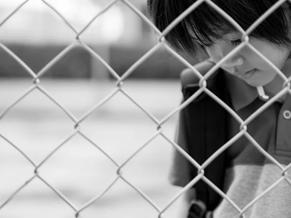 Svart och vitt ledsen pojke bakom staket mesh nät. Känslor koncept - sorg, sorg, melankoli. — Stockfoto
