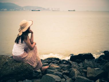 Issız bir kumsal denizde önünde oturan bir sonbahar gününde retro yalnız ve depresyonda kadın.