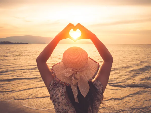 Ładna kobieta, trzymając się za ręce w sercu kształt oprawy ustawienie podczas zachodu słońca na ocean plaża — Zdjęcie stockowe