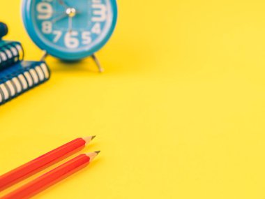 Not defterleri, kırmızı kalem ve Sarı zemin üzerine çalar saat gibi ofis aksesuarları. Eğitim ve iş kavramı.