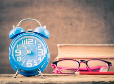 Retro ofis aksesuarları kitap, kırmızı kalem, pembe gözlük ve çalar saat ahşap arka plan üzerinde de dahil olmak üzere. Eğitim ve iş kavramı.