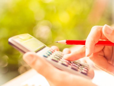 kadın el hesap makinesi ve holding kırmızı kalem, doğa yeşil yaprakları arka plan tabloyla çalışma iş belge ve Not Defteri ile çalışma.