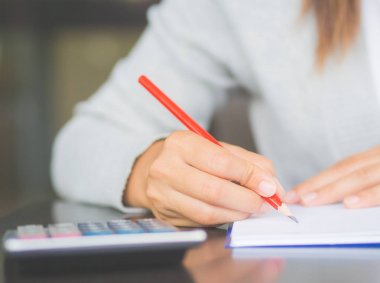 Kadın el kırmızı kalem ve hesap makinesi ile çalışma tablosu üzerinde yazma. İş ve eğitim kavramı.