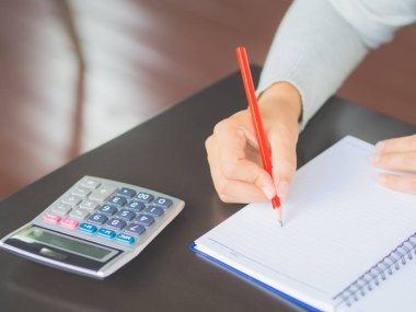 Kadın el kırmızı kalem ve hesap makinesi ile çalışma tablosu üzerinde yazma. İş ve eğitim kavramı.
