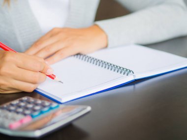 Kadın el kırmızı kalem ve hesap makinesi ile çalışma tablosu üzerinde yazma. İş ve eğitim kavramı.