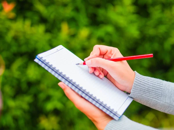 Vrouw hand met rood potlood schrijven op notebook in landbouw tuin. — Stockfoto
