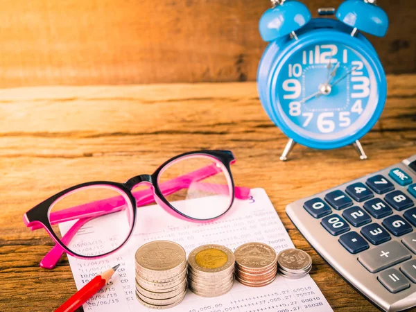 Retro stack of coins with calculator, red pencil and alarm clock on wooden background. Business Finance and time of money concept.