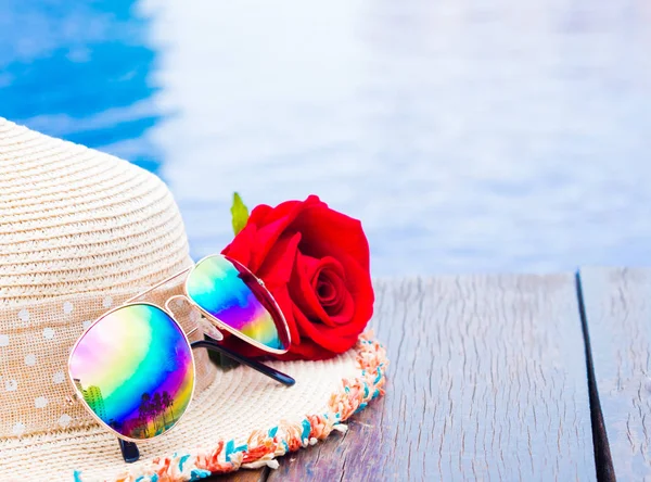 Flores rosas rojas con sombrero de verano y gafas de sol junto a la piscina. Vacaciones y relajación, concepto de viaje de verano . — Foto de Stock