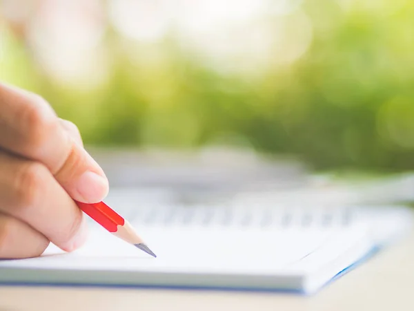 Closeup vrouw hand schrijven met rood potlood, zakelijke document en nota boek over werktafel met natuur groene bladeren achtergrond. — Stockfoto