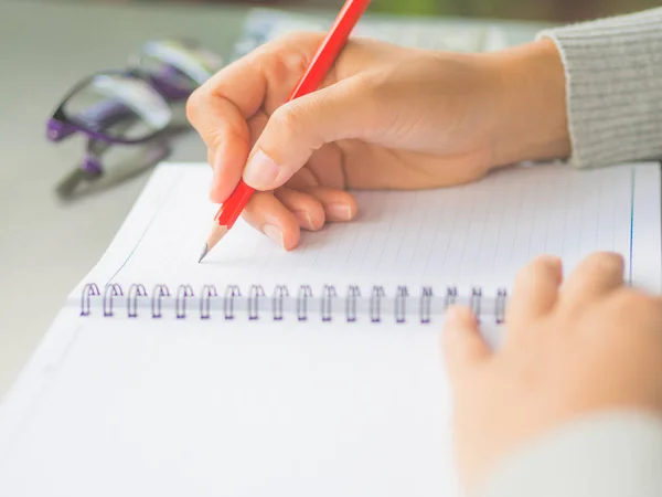 Närbild kvinna hand skriver med röd penna och glasögon bakgrund på arbetsbord. — Stockfoto