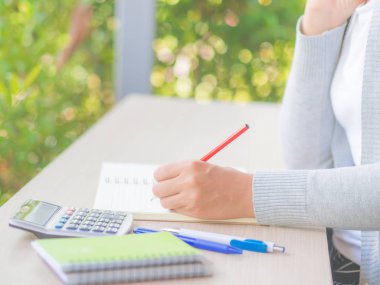 Kadın el beyaz kalem, kırmızı kalem ve hesap makinesi ile çalışma tablosu ve ağaç yazılı arka plan bırakır. İş ve eğitim kavramı.