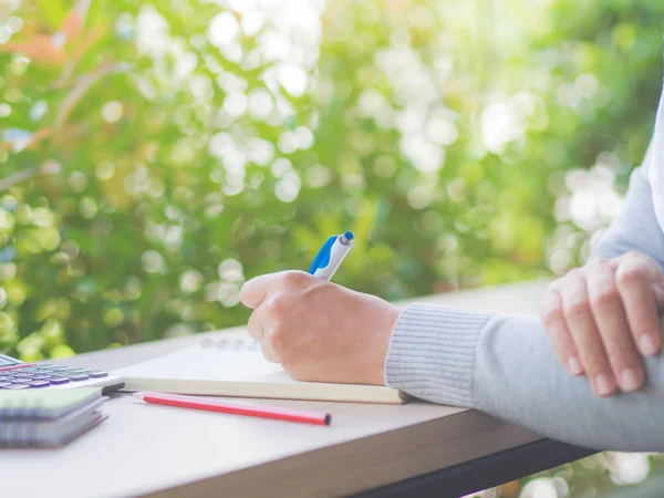 Kvinna hand skriver med vit penna, röd penna och kalkylator på arbetsbordet och tree löv bakgrund. Business och education koncept. — Stockfoto