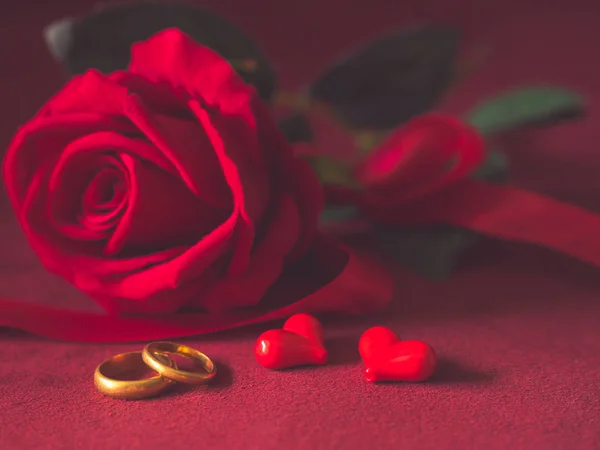 Chiave bassa primo piano di anelli di fidanzamento e rose rosse su sfondo rosa. Amore, proposta, giorno di San Valentino e vacanze concetto . — Foto Stock