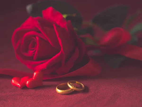 Chiave bassa primo piano di anelli di fidanzamento e rose rosse su sfondo rosa. Amore, proposta, giorno di San Valentino e vacanze concetto . — Foto Stock