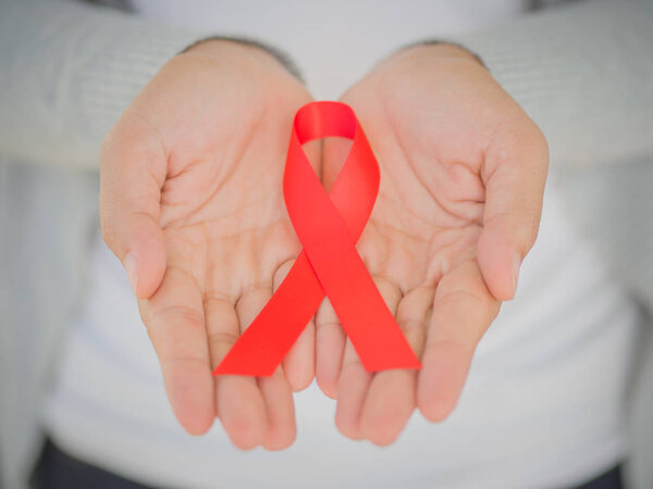 Руки женщины крупным планом держат красную ленточку ВИЧ, ленту для информирования о СПИДе во всем мире. Здравоохранение и медицина
. 