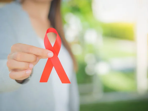 Primer plano mujer mano sosteniendo cinta roja VIH, cinta de sensibilización Día Mundial del SIDA. Concepto de salud y medicina . — Foto de Stock