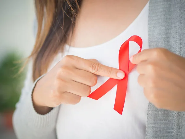 Primeros planos de la mano de una mujer con cinta roja de sensibilización sobre el sida. Concepto de salud y medicina . — Foto de Stock