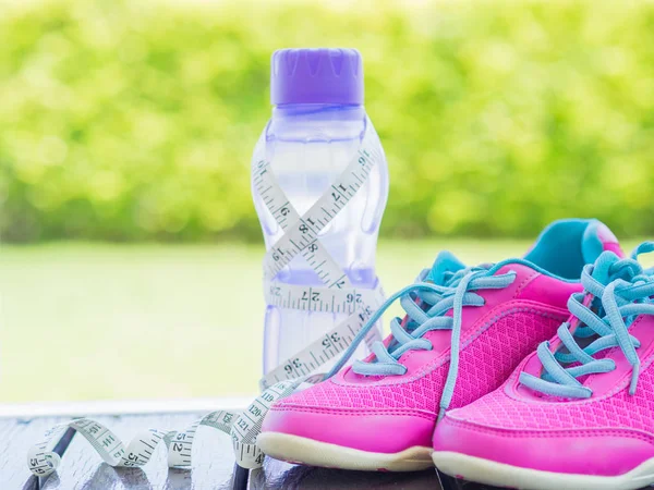 Pair of pink sport shoes and water bottle with green bokeh.