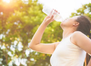 Mutlu güzel genç kadın içme su şişe ağaç arka plan bırakın. Sağlık kavramı.