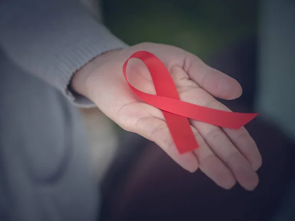 Primeros planos de las manos femeninas con cinta roja VIH, cinta de sensibilización del Día Mundial del Sida. Concepto de salud y medicina . — Foto de Stock
