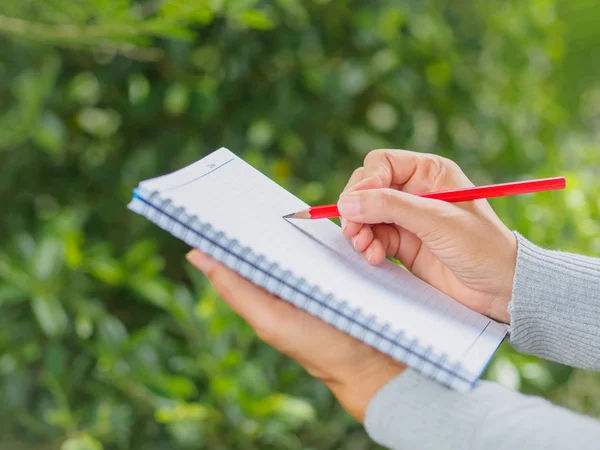 Woman hand with red pencil writing on notebook — Stock Photo, Image