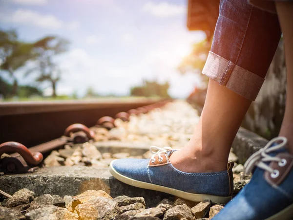 Closeup žena nohy v modré tenisky sedí železnice. — Stock fotografie