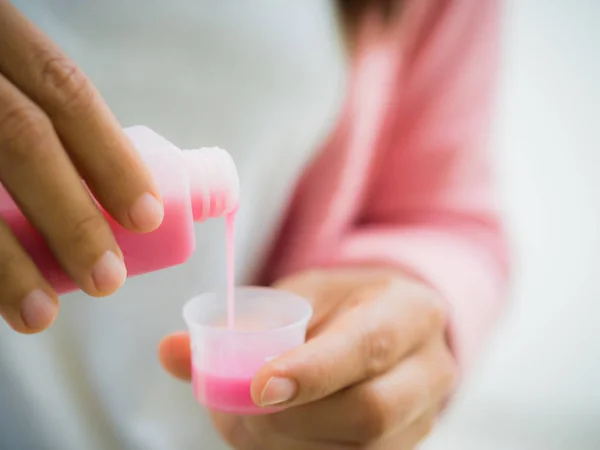 Closeup woman pouring medication or antipyretic syrup from bottle to cup. — Stock Photo, Image