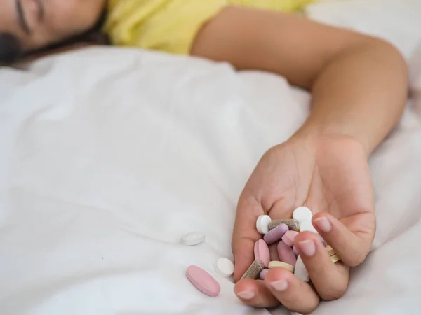 Jovem mulher está deitada na cama com um monte de comprimidos . — Fotografia de Stock