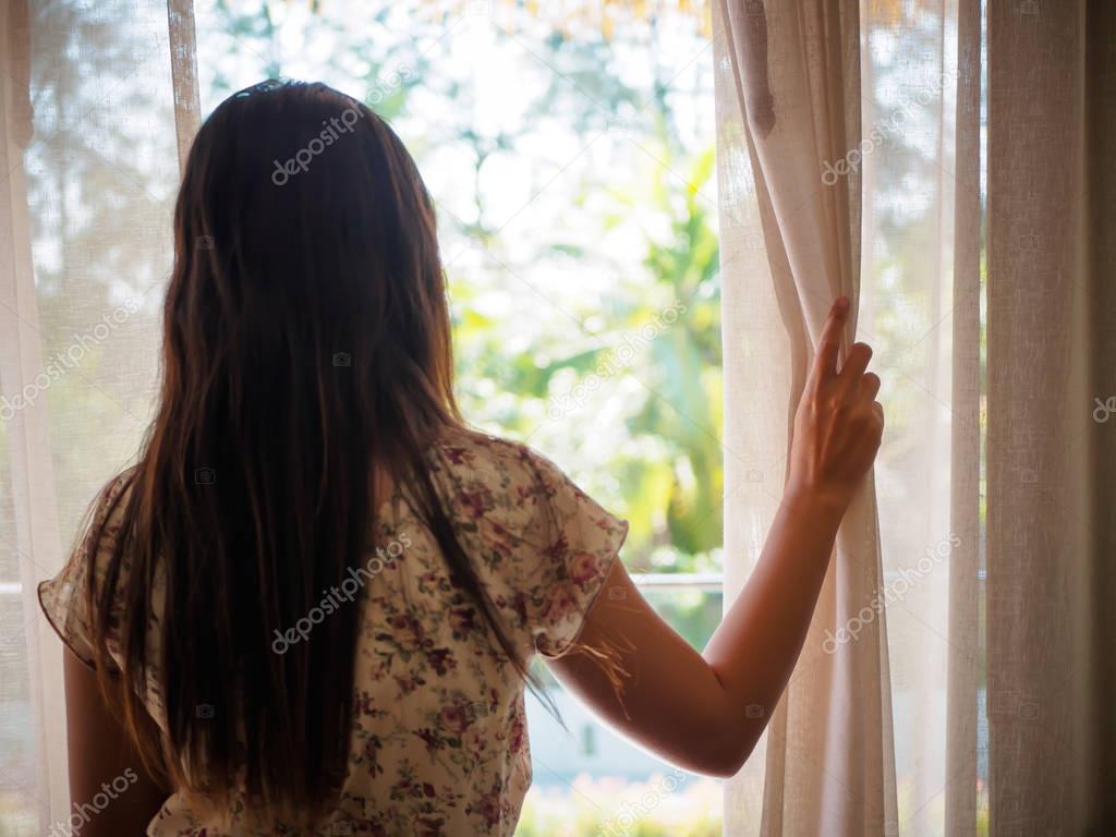Young woman holding the curtains open to looking through the window