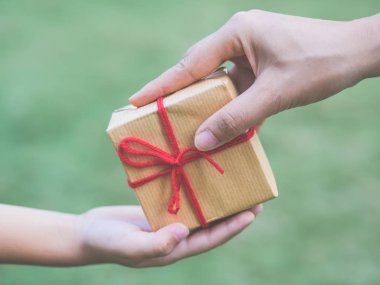 Çocuk ve anne ellerin hediye kutusu ile yeşil arka plan üzerinde yakın çekim.