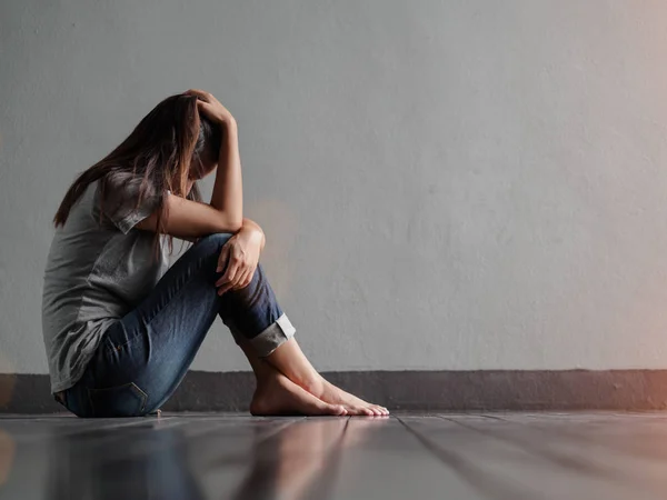 Mujer triste abrazar su rodilla y llorar mientras está sentado solo en una habitación vacía —  Fotos de Stock