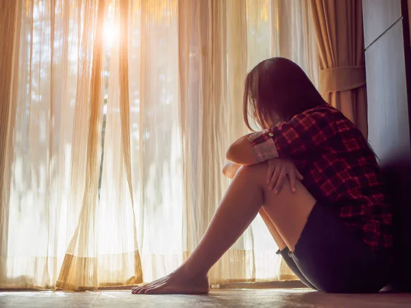 Sorgliga kvinnan krama henne knä och gråta. När man sitter ensam i ett tomt rum bredvid fönster eller dörr. — Stockfoto
