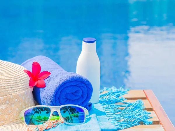 Gafas de sol, sombrero de playa, toalla azul y protector solar al lado de la piscina . — Foto de Stock