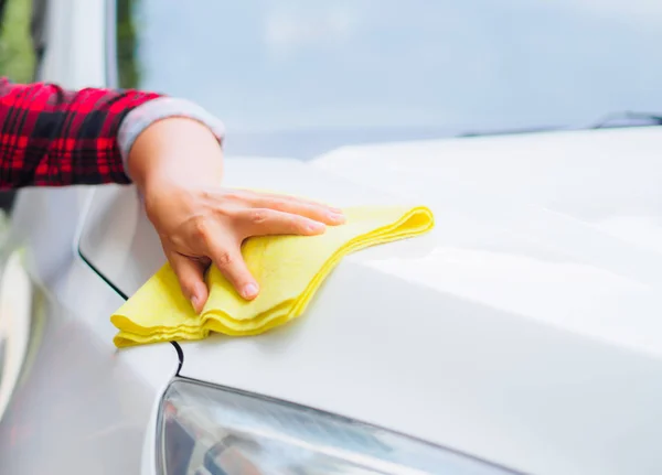 Ruka s žlutým microfiber hadřík čištění bílé auto. — Stock fotografie