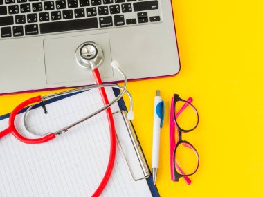 Stetoskop, kalem ve gözlük ile sarı arka plan üstünde laptop.