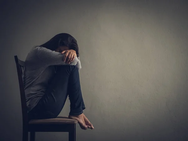 Depressive Frau sitzt zu Hause auf einem Stuhl im dunklen Raum. — Stockfoto