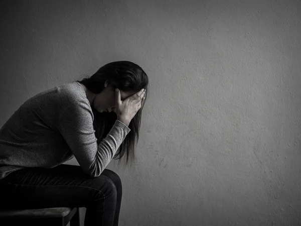 Depressed woman sitting on a chair in dark room at home. — Stock Photo, Image