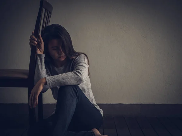 Mujer deprimida sentada en el suelo cerca de una silla en habitación oscura —  Fotos de Stock