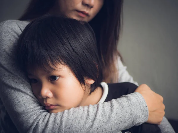 Fechar triste menino sendo abraçado por sua mãe em casa . — Fotografia de Stock