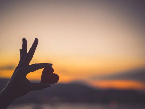 Σιλουέτα χέρι κρατά όμορφη καρδιά κατά τη διάρκεια του ηλιοβασιλέματος φόντο — Φωτογραφία Αρχείου