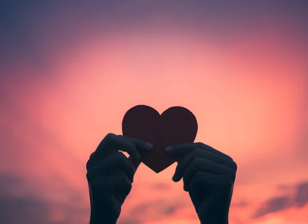 Sırasında günbatımı arka plan kırmızı kalp tutan Closeup el. 
