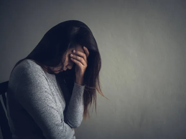 Depressed woman sitting on a chair in dark room at home. — Stock Photo, Image