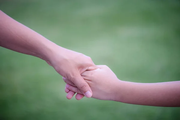Mor en hand av hans son med grönt glas bakgrund. Kärlek, familjeförmåner och mor dag koncept. — Stockfoto
