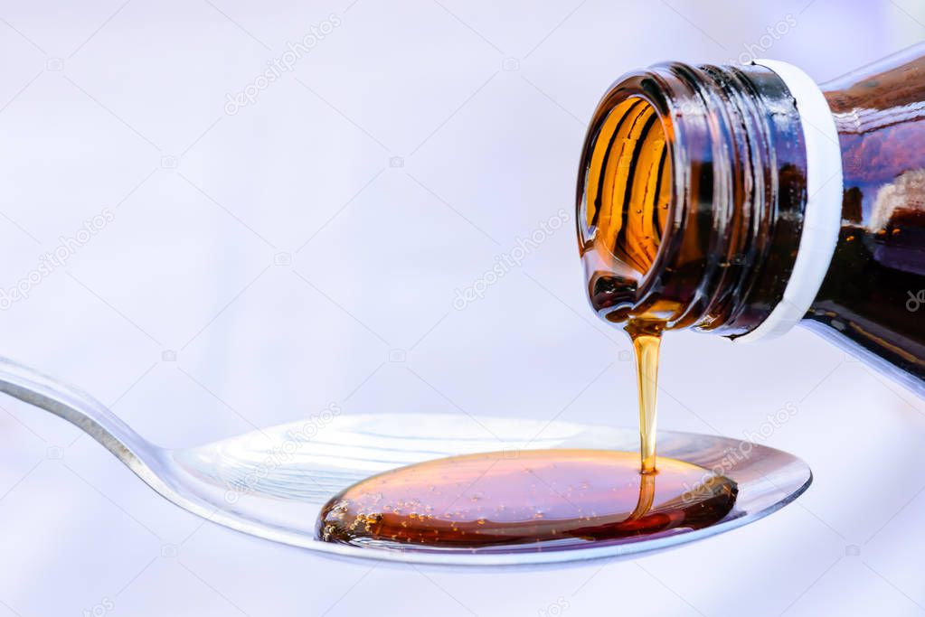 Hand pouring medication or antipyretic syrup from bottle to spoon