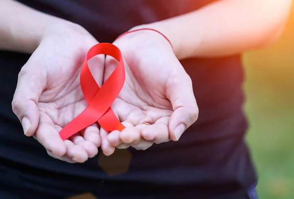 Manos de mujer sosteniendo cinta roja de conciencia del SIDA . — Foto de Stock