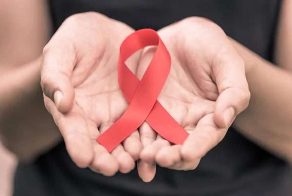 Manos femeninas sosteniendo cinta roja de sensibilización sobre el sida . — Foto de Stock