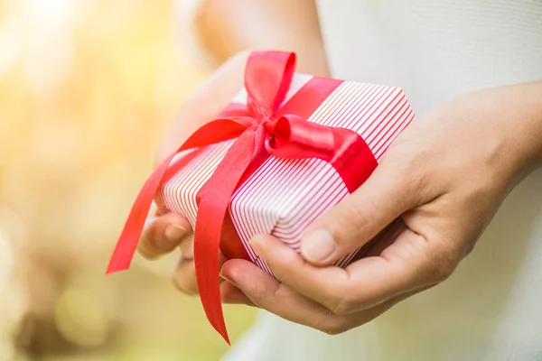 Mano femminile in possesso di una confezione regalo con nastro rosso . — Foto Stock