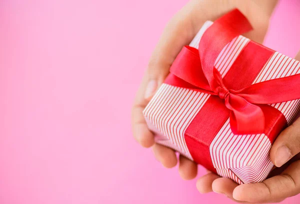 Mano che tiene una scatola regalo rossa su sfondo rosa  . — Foto Stock
