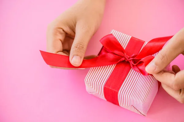 Mano che tiene una scatola regalo rossa su sfondo rosa  . — Foto Stock